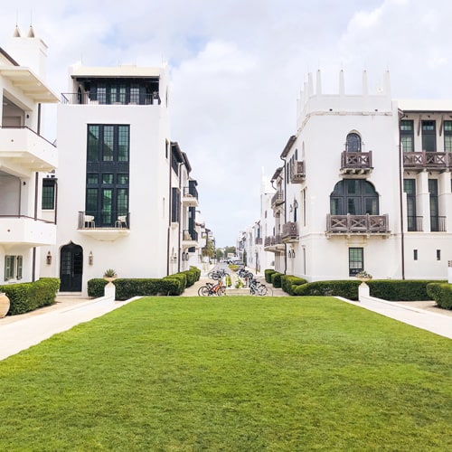 Green, square lawn lined looking towards a street lined with white buildings with black and brown shutters and balconies