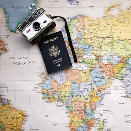 Pastel-colored map of the world with a passport and a camera sitting on top of the map