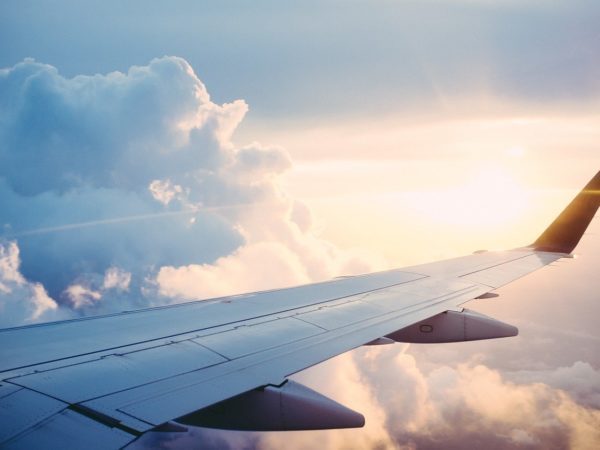 View of a silver airplane wing next to a large cloud, with the sun setting in a soft golden light