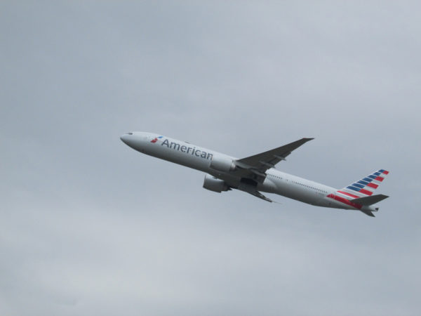 American Airlines plane with a red, white, and blue flag on the tail flies through a grey sky