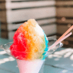 snow cone with red, yellow, and blue syrup on a picnic table
