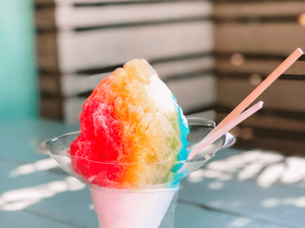 snow cone with red, yellow, and blue syrup on a picnic table